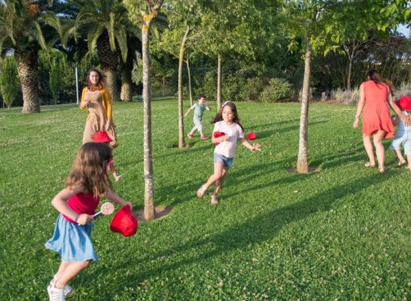 Kids and adults enjoy playing together in a lush, sunny park setting.